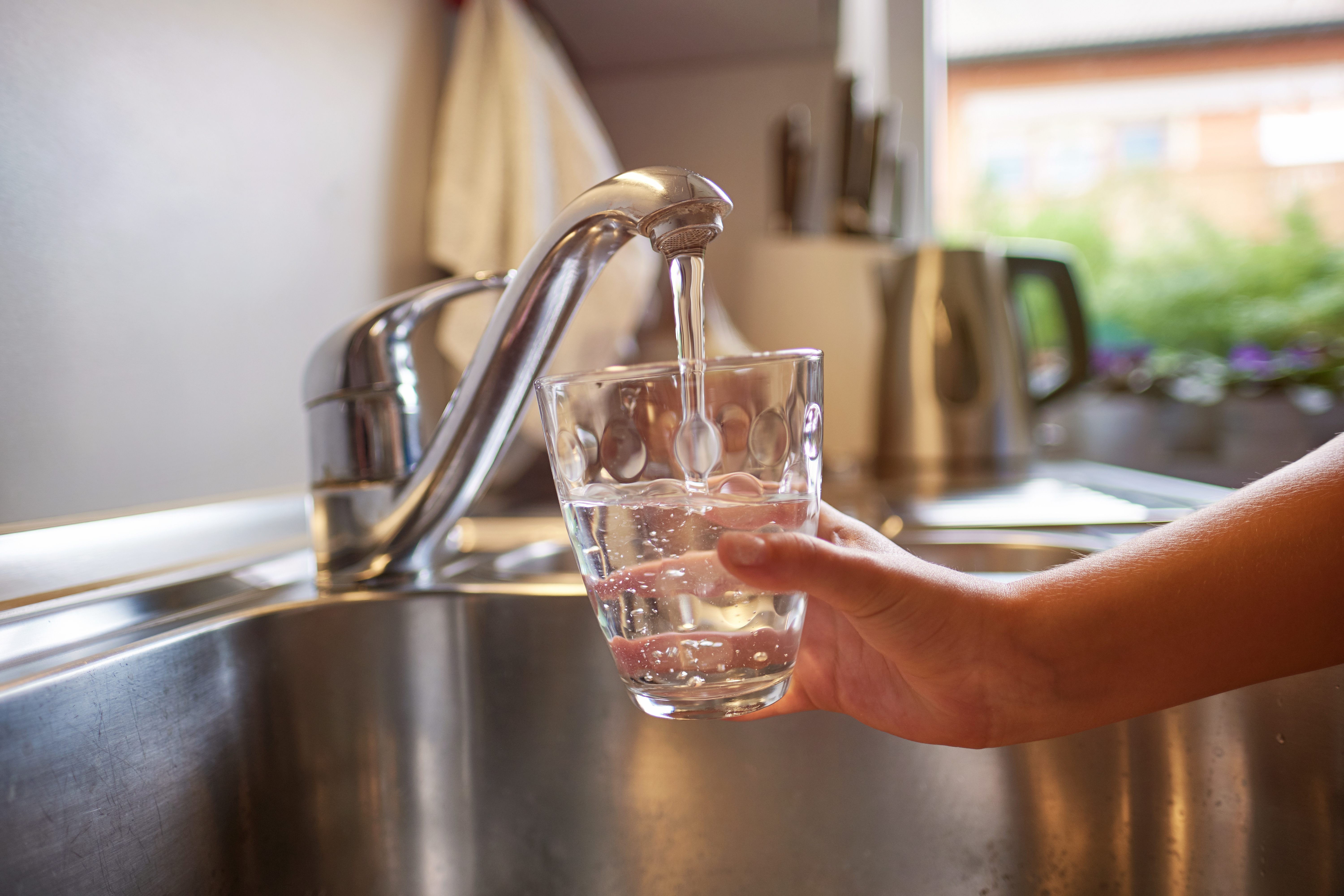 Kinderhand, die sich am Wasserhahn frisches Wasser in ein Glas gießt