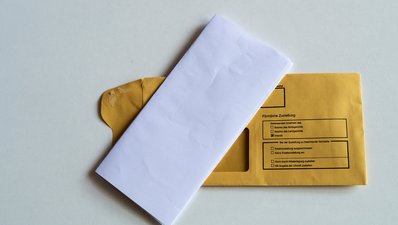 Ein gefalteter Briefbogen liegt auf einem Kuvert, auf dem Persönliche Zustellung steht.