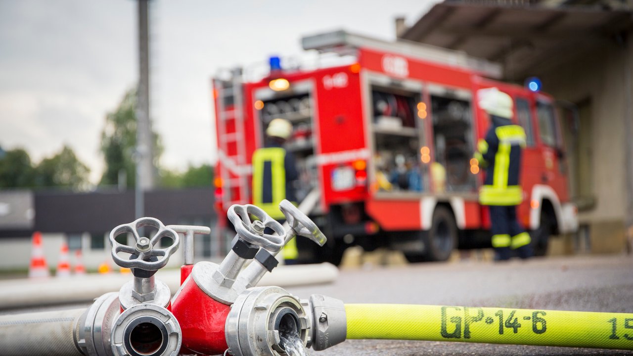 Bild zeigt Feuerwehrschlauch mit Feuerwehrfahrzeug im Hintergrund