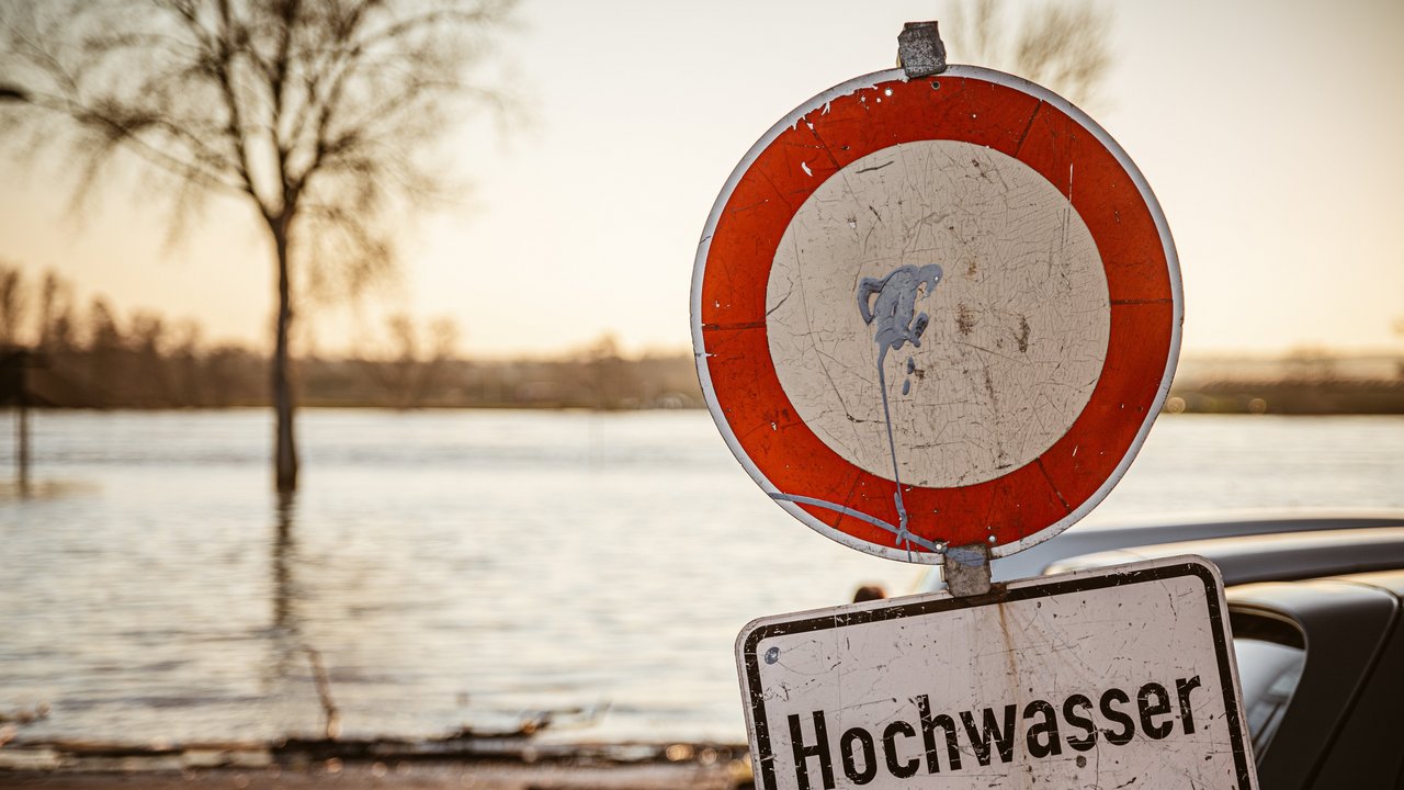 Bild zeigt einen Fluß mit einem Schild auf dem "Hochwasser" steht