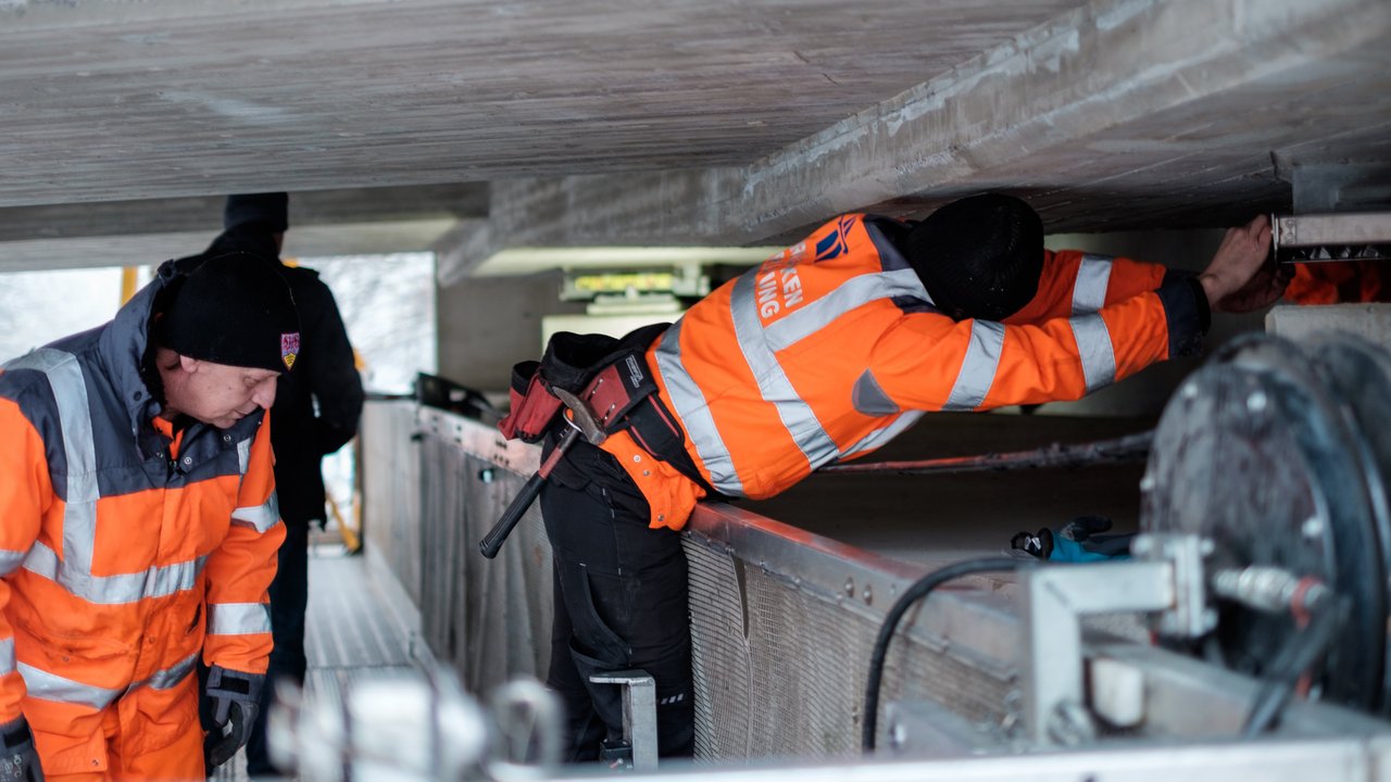 Zwei Arbeiter prüfen eine Brücke von unten Zwei Arbeiter prüfen eine Brücke von unten