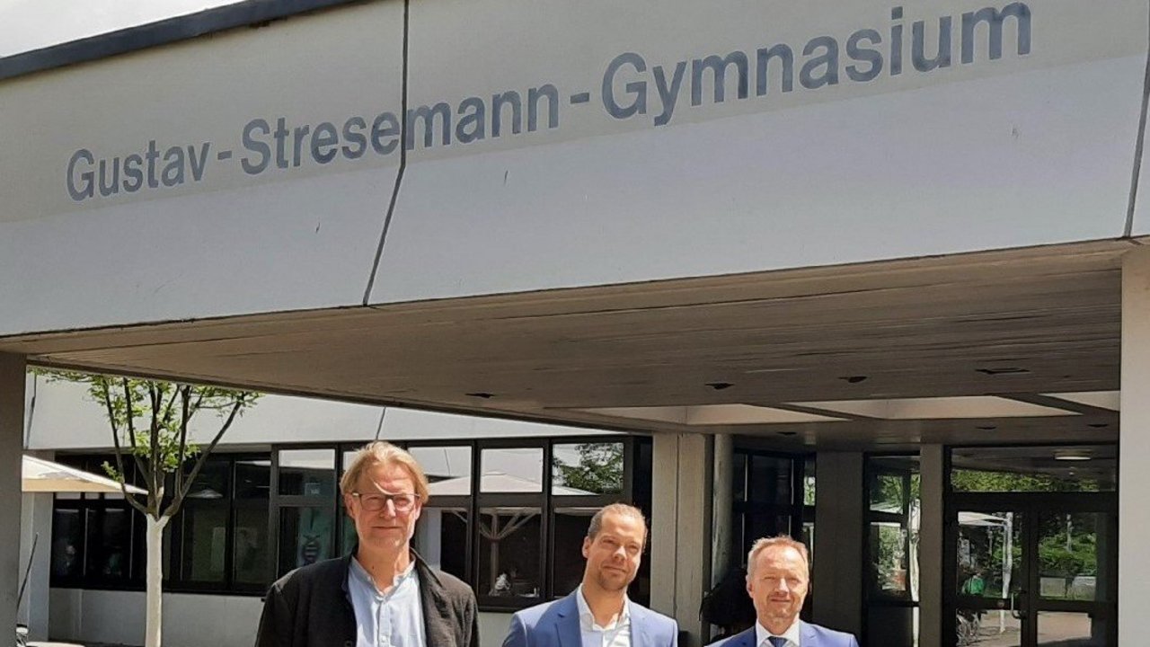 Bild zeigt Dr. Thomas Hölz und Armin Dunz bei der Überreichung des Bestellungsschreibens an Daniel Meier vor dem Gustav-Stresemann-Gymnasium