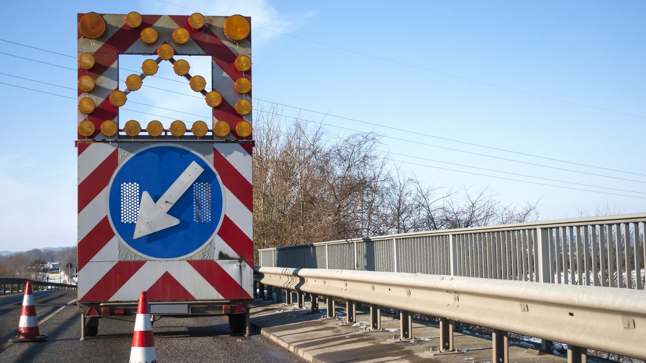 Baustelle auf einer Brücke mit Baustellenfahrzeug und Warnschild, Fahrbahnverengung