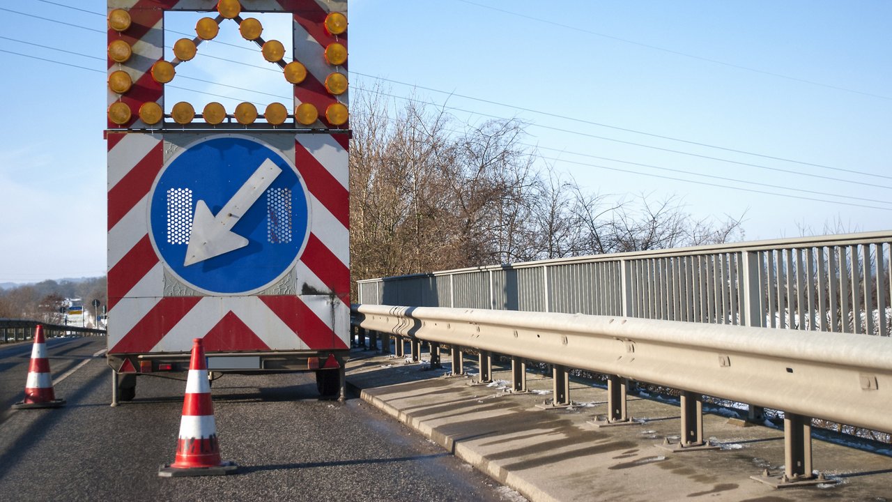 Baustelle auf einer Brücke mit Baustellenfahrzeug und Warnschild, Fahrbahnverengung