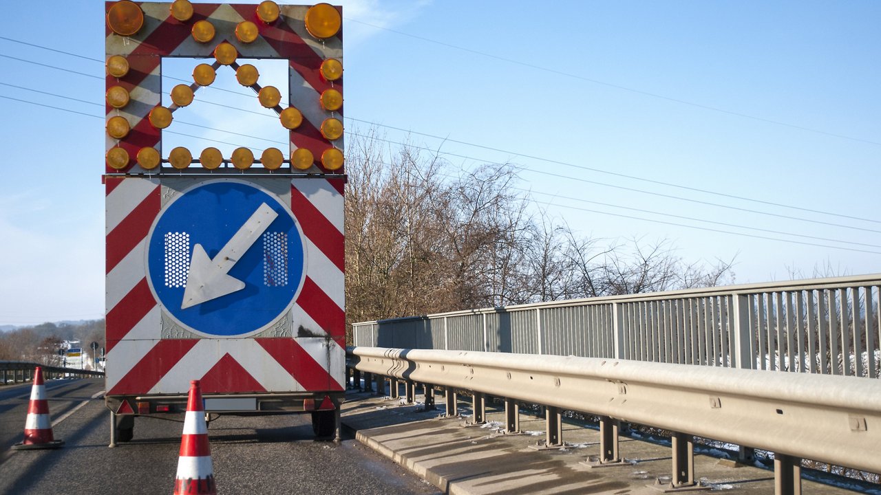 Baustelle auf einer Brücke mit Baustellenfahrzeug und Warnschild, Fahrbahnverengung