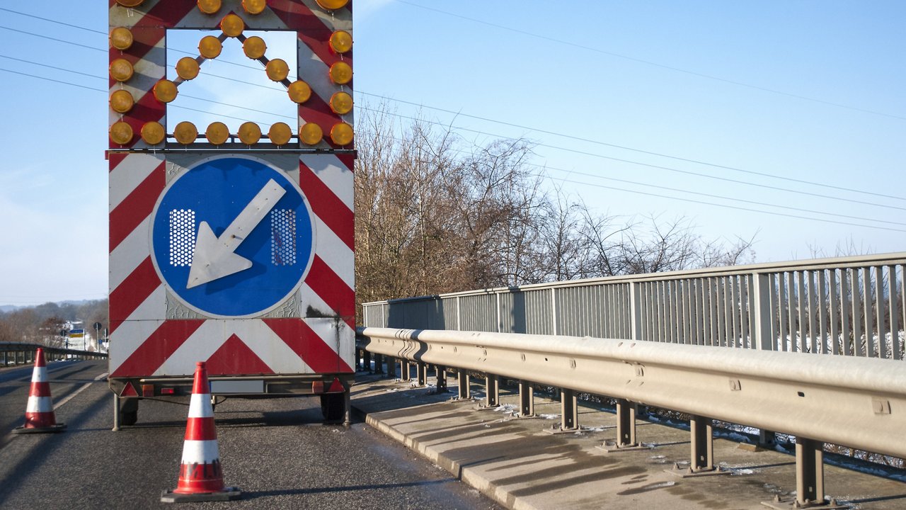Baustelle auf einer Brücke mit Baustellenfahrzeug und Warnschild, Fahrbahnverengung