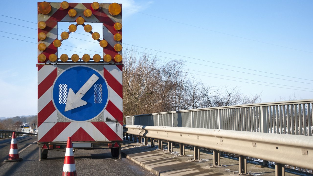 Baustelle auf einer Brücke mit Baustellenfahrzeug und Warnschild, Fahrbahnverengung