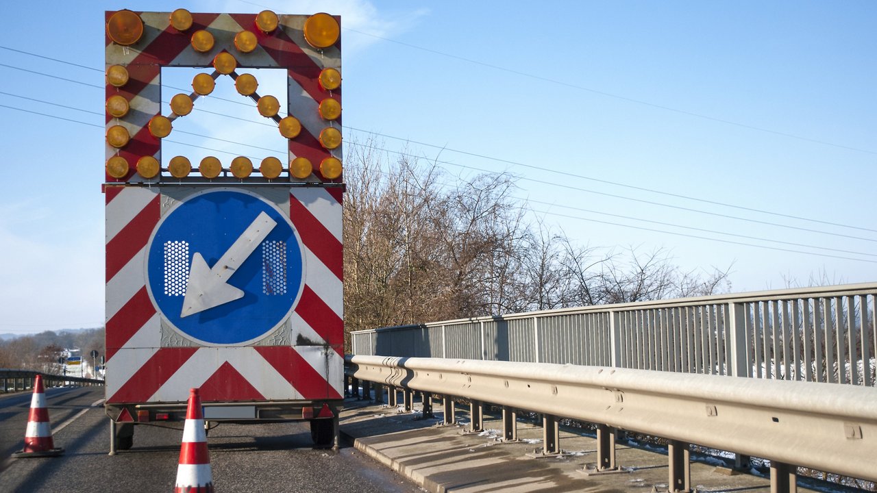 Baustelle auf einer Brücke mit Baustellenfahrzeug und Warnschild, Fahrbahnverengung