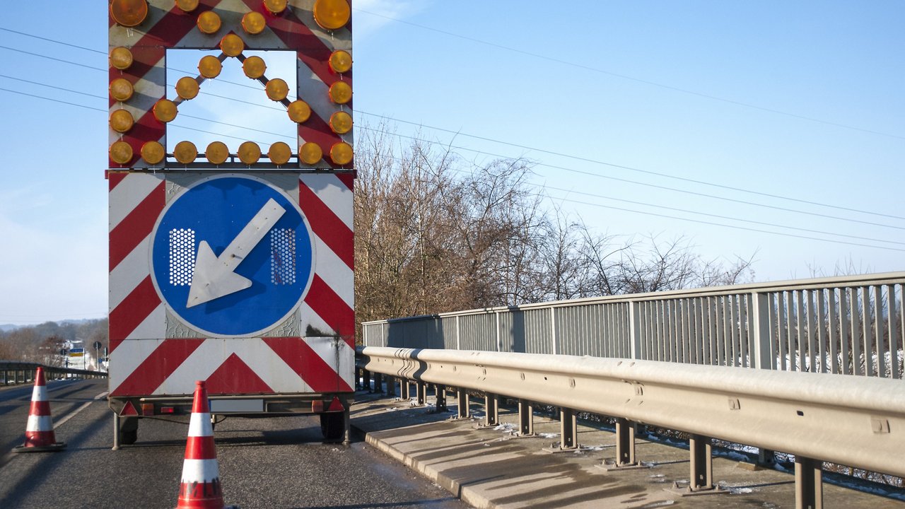 Baustelle auf einer Brücke mit Baustellenfahrzeug und Warnschild, Fahrbahnverengung