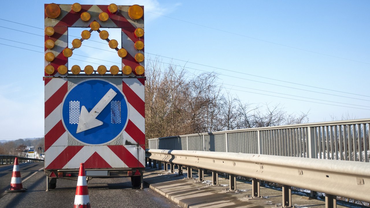 Baustelle auf einer Brücke mit Baustellenfahrzeug und Warnschild, Fahrbahnverengung Baustelle auf einer Brücke mit Baustellenfahrzeug und Warnschild, Fahrbahnverengung