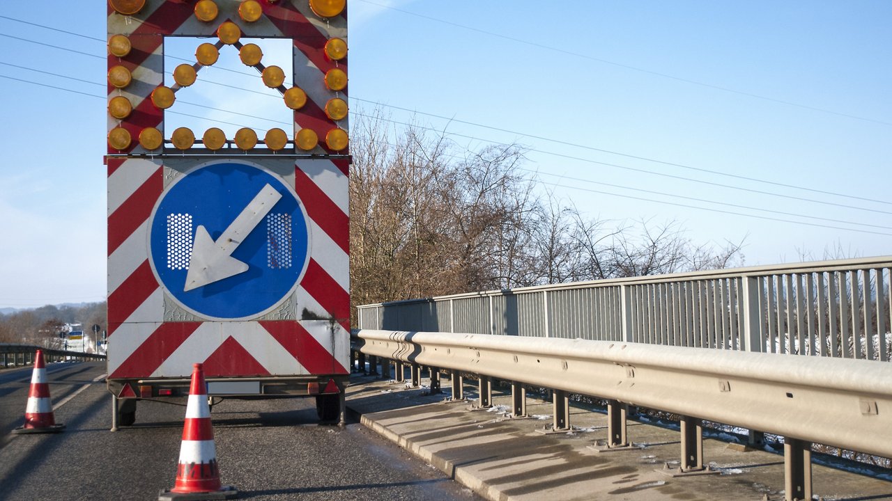 Baustelle auf einer Brücke mit Baustellenfahrzeug und Warnschild, Fahrbahnverengung
