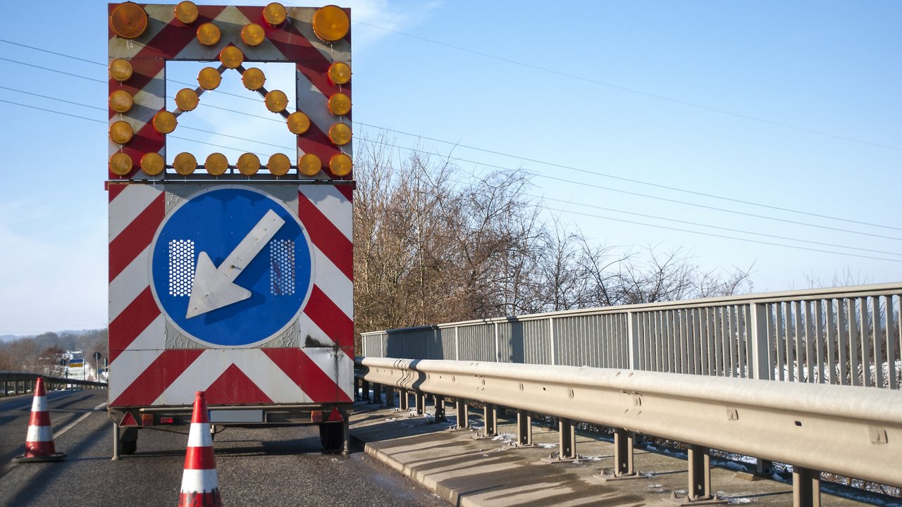 Baustelle auf einer Brücke mit Baustellenfahrzeug und Warnschild, Fahrbahnverengung