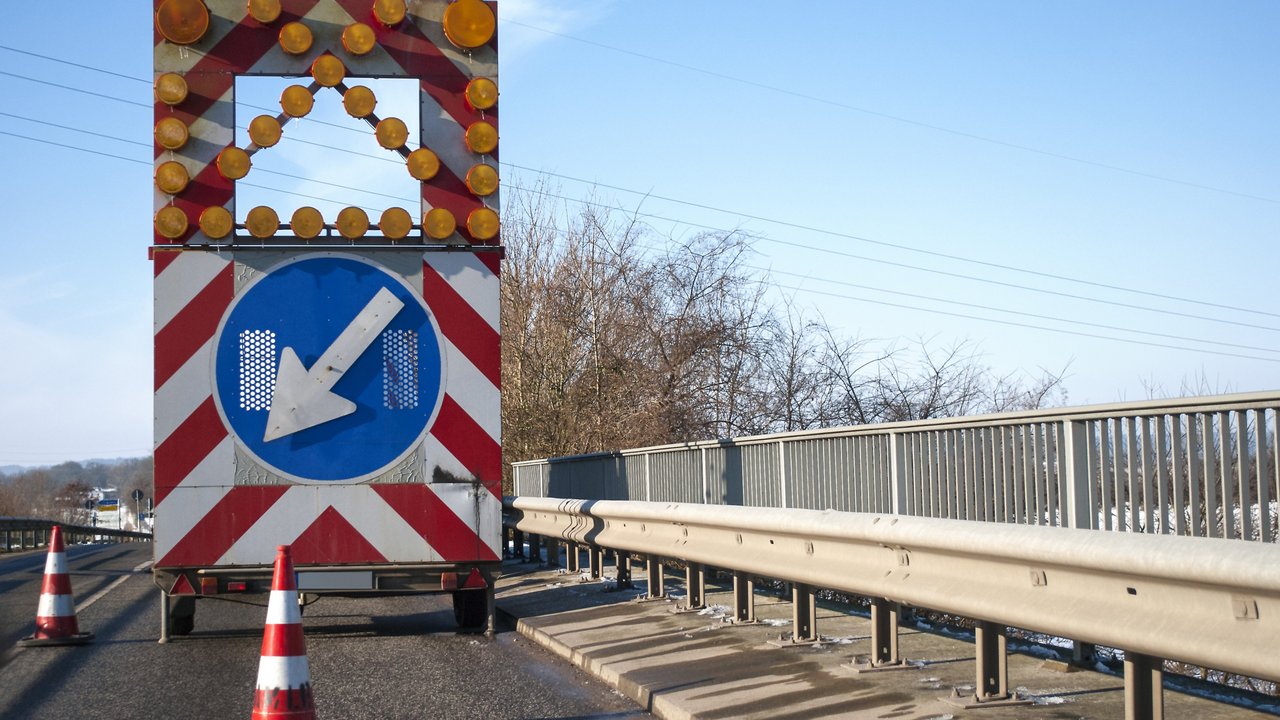Baustelle auf einer Brücke mit Baustellenfahrzeug und Warnschild, Fahrbahnverengung
