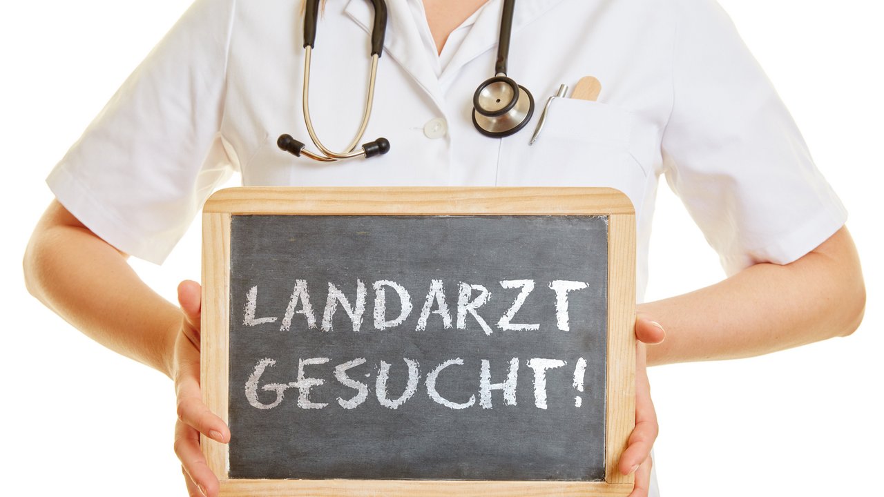 Person hält Kreidetafel mit der Aufschrift "Landarzt gesucht"