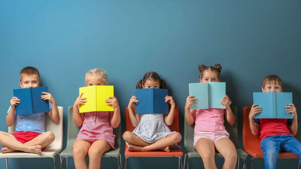 Schulkinder sitzen vor einer farbigen Wand und lesen Bücher