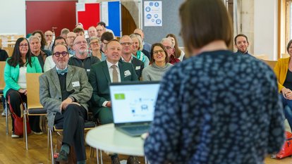 Eine Frau hält einen Vortrag vor mehreren Personen mit Hilfe eines Laptops