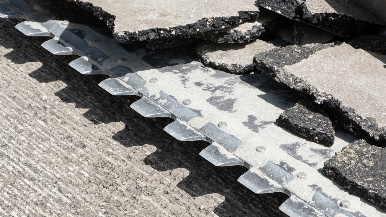 Baggerschaufel mit Stücken gebrochenen Asphalts entfernt Straßenbelag