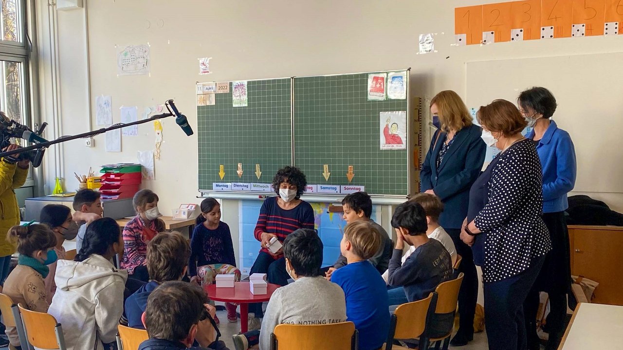 Kultusministerin Theresa Schopper (stehend, mitte), die Bürgermeisterin für Jugend und Bildung der Stadt Stuttgart, Isabel Fezer (stehend, links), und Regierungspräsidentin Susanne Bay (stehend, rechts) in einer Vorbereitungsklasse der Ameisenbergschule.