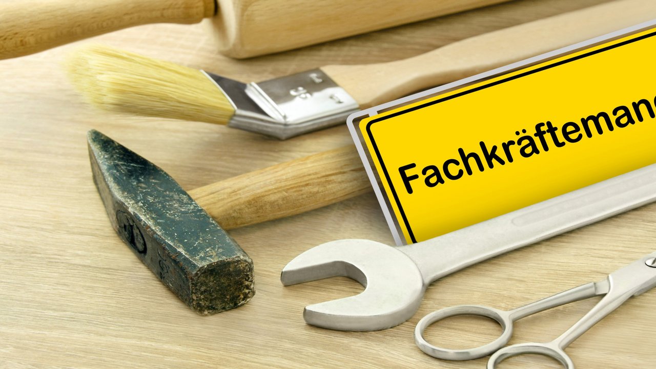 Gelbes Schild "Fachkräftemangel" in Deutschland mit Werkzeugen auf Holz