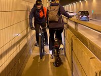 Zwei Fahrradfahrer begegnen sich auf einem sehr schmalen Fahrradweg im Flughafentunnel.