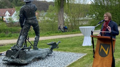 Frau Bürgermeisterin Braun steht am Rednerpult und hält Ihre Brüßungsrede, dahinter Stehtische, neben Ihr eine Skulptur