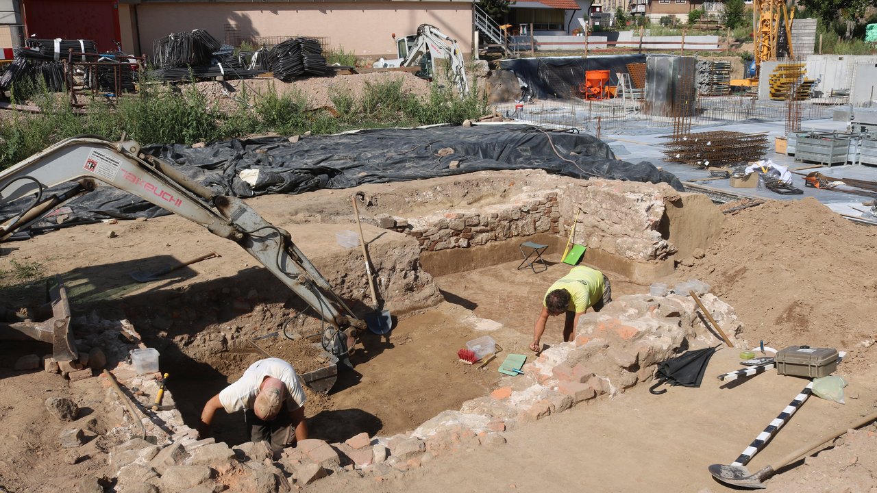 Bild zeigt wie Archäologen den Keller untersuchen, im Hingrund Bauarbeiten