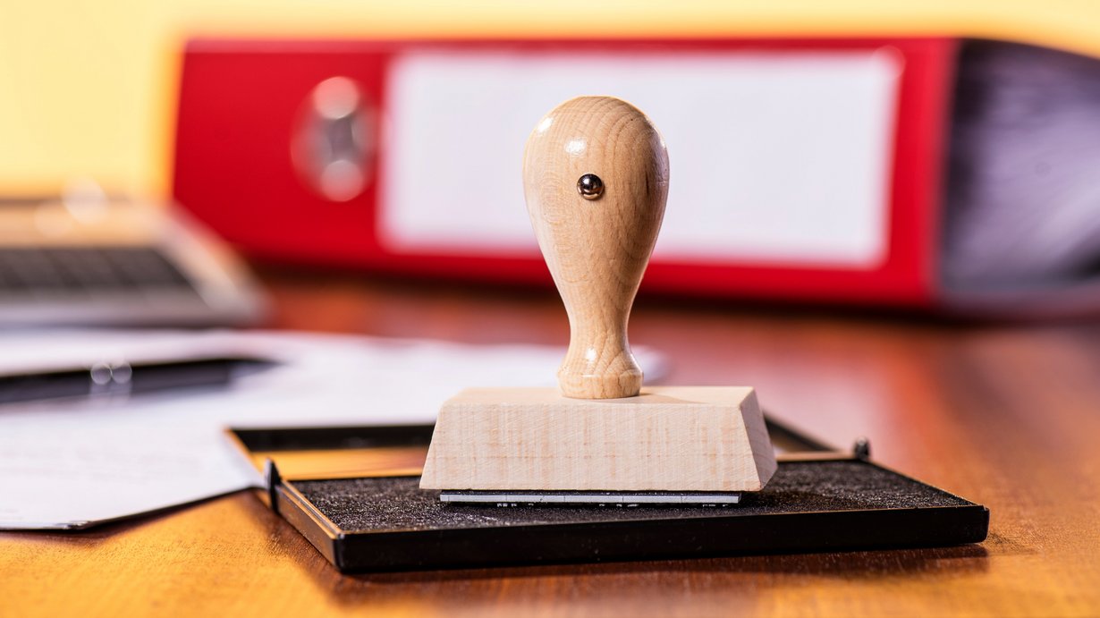 Stempelkissen mit Stempel und rotem Ordner im Hintergrund