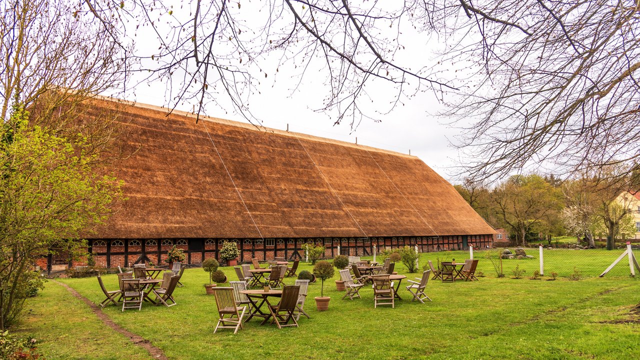 Bild zeigt Tische und Stühle vor einem Gasthaus auf einer Wiese