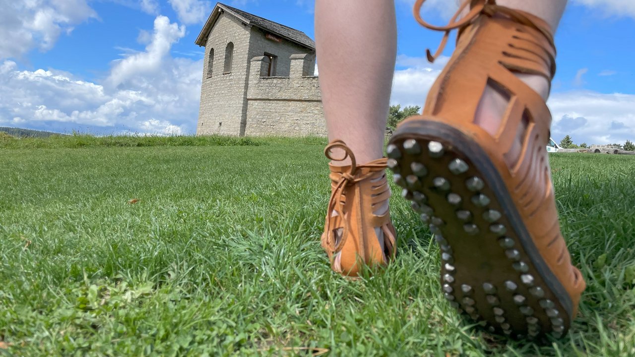 Bild zeigt römischen Soldatenstiefel (lateinisch: caliga) mit genagelter Sohle. Im Hintergrund der 1975 nachgebaute Eckturm des Kastells Waldmössingen 