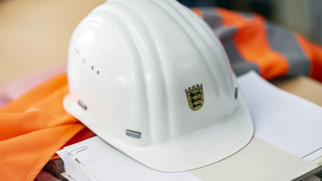 Auf einer Sicherheitsweste und auf einem Papierstapel liegt ein Bauhelm