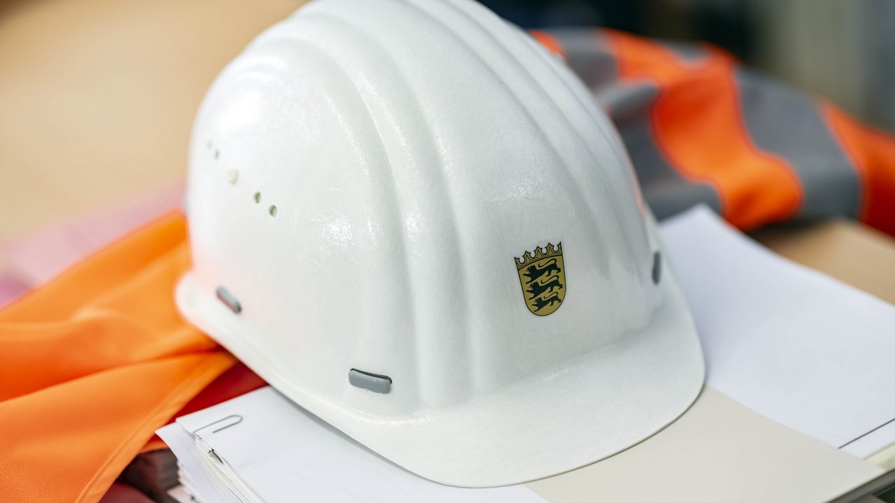 Auf einer Sicherheitsweste und auf einem Papierstapel liegt ein Bauhelm