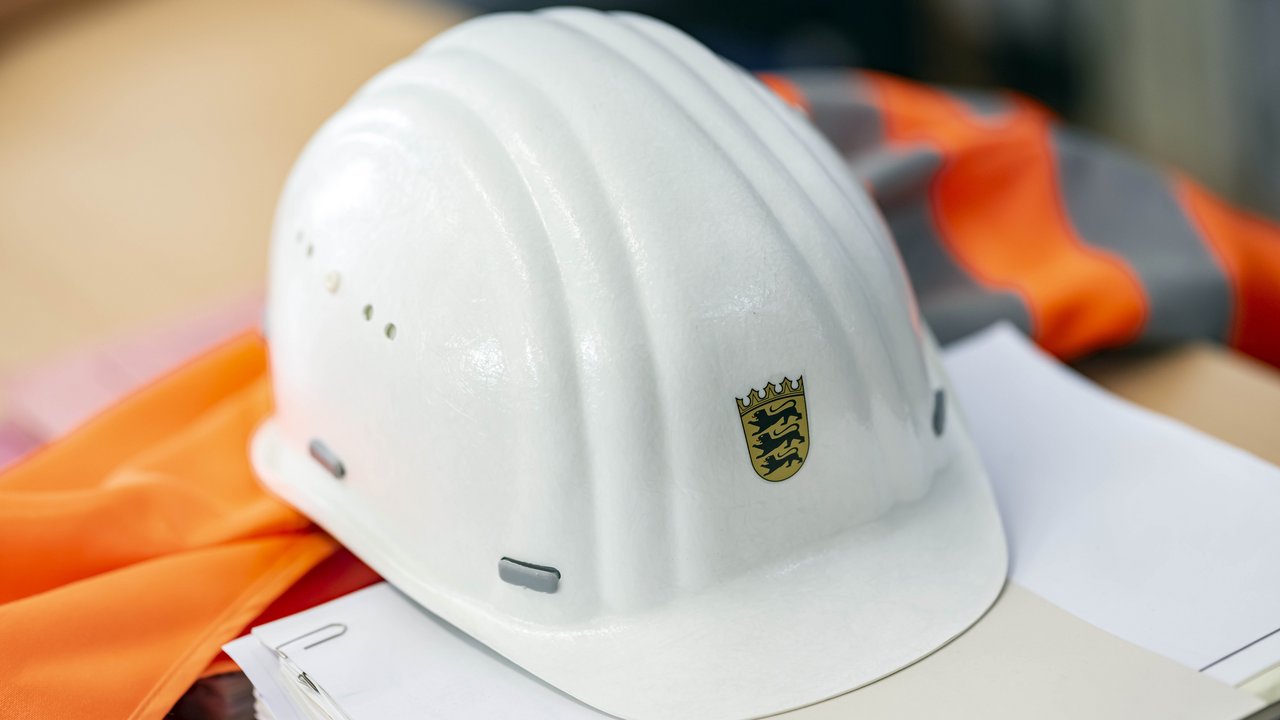 Auf einer Sicherheitsweste und auf einem Papierstapel liegt ein Bauhelm