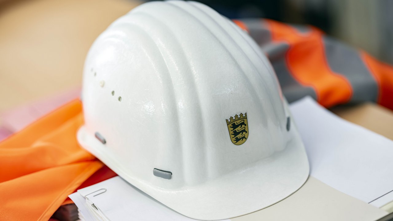 Auf einer Sicherheitsweste und auf einem Papierstapel liegt ein Bauhelm