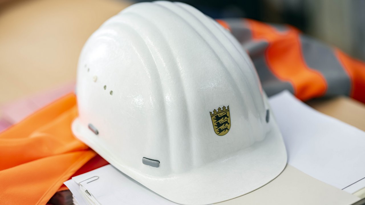 Auf einer Sicherheitsweste und auf einem Papierstapel liegt ein Bauhelm