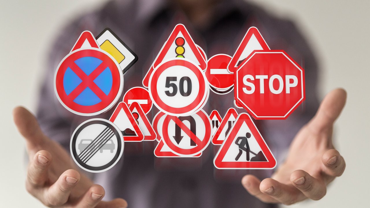 Mann hält verschiedene Verkehrsschilder zwischen seinen Händen