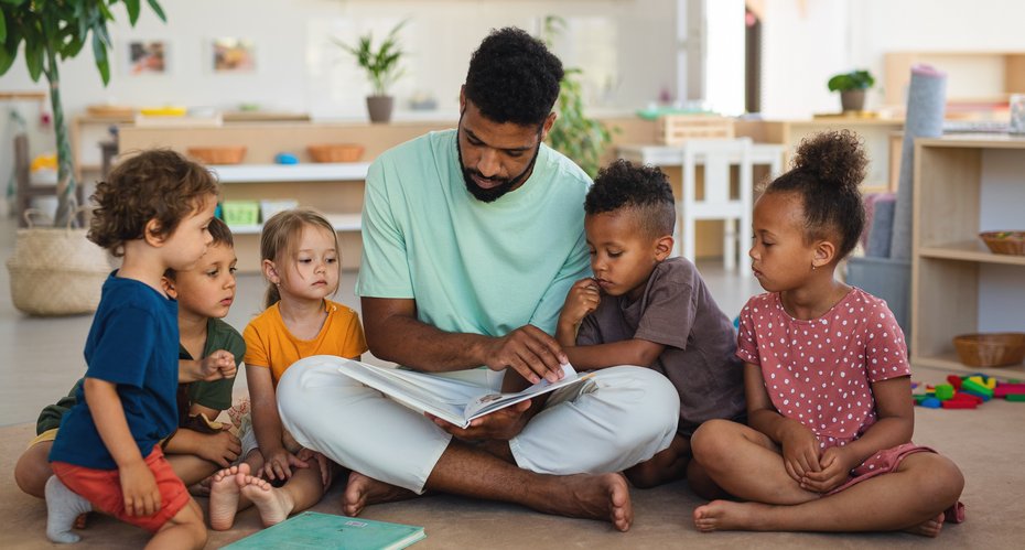 Mann liest Kindern vor, sitzend auf dem Boden