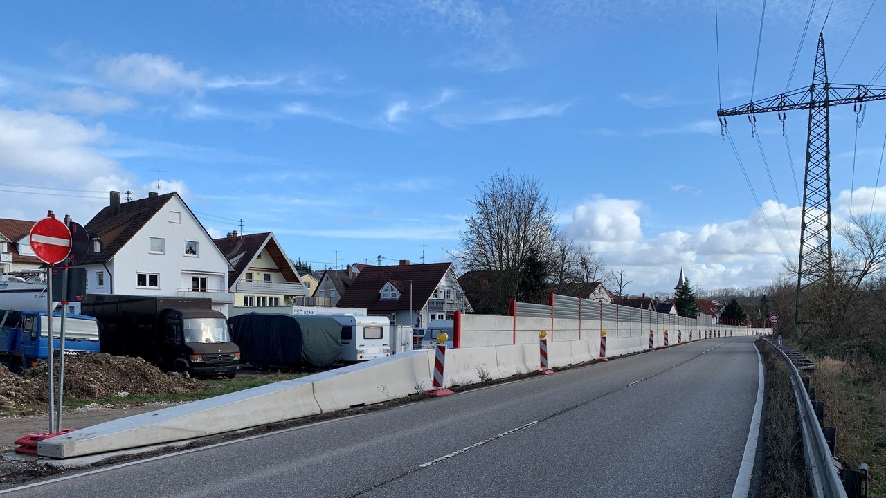 Lärmschutzwand entlang einer Straße, dahinter Häuser