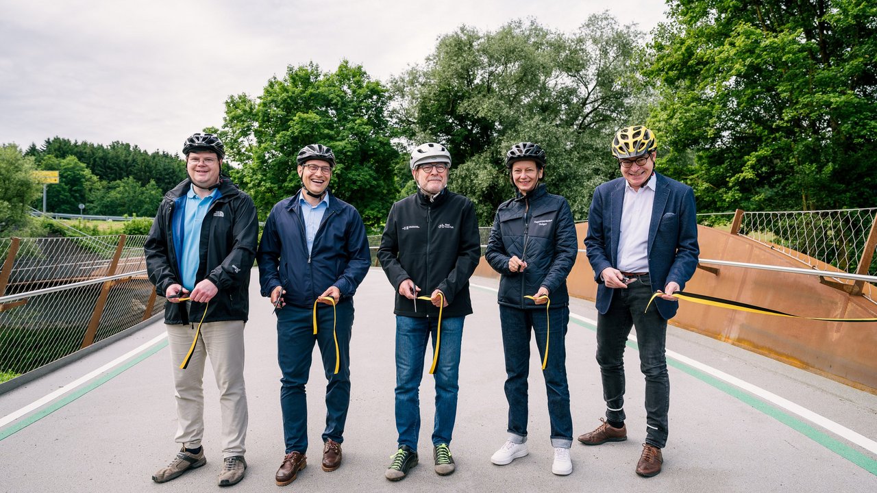 Gemeinsam mit Bürgermeister Eberhard Keller (Ebersbach), Landrat Marcel Musolf (Esslingen), Verkehrsminister Winfried Hermann und Landrat Edgar Wolff (Göppingen) (v.l.n.r) gab Regierungspräsidentin Susanne Bay die Strecke für den Radverkehr frei. Eberhard Keller, Marcel Musolf, Winfried Hermann, Susanne Bay und Edgar Wolff stehen gemeinsam auf einer Brücke. Sie halten gelbe Bänder in der Hand und haben alle Radhelme auf.