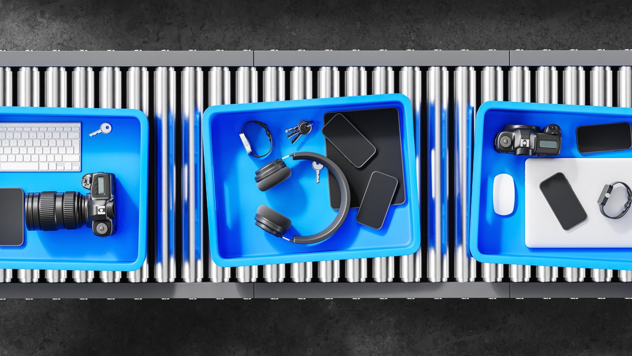 Bild zeigt Boxen mit elektronischen Geräten und persönlichen Gegenständen an der Sicherheitskontrolle am Flughafen