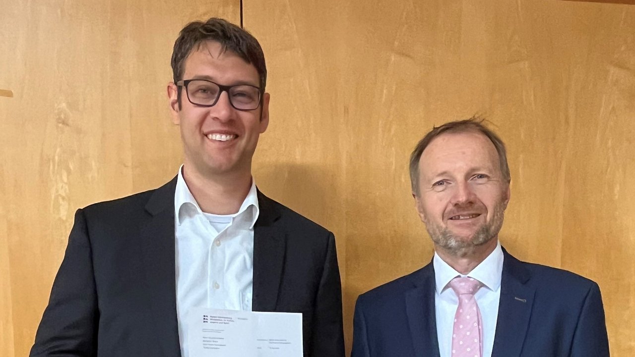 Dr. Thomas Hölz (rechts), Leiter des Gymnasialreferats am Regierungspräsidium Stuttgart, überreicht Benjamin Brack (links) das Bestellungsschreiben von Kultusministerin Theresa Schopper. Quelle: Friedrich-Schiller-Gymnasium Fellbach