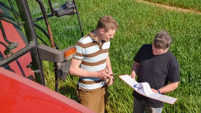 Ein Landwirt und ein Prüfer vor einem Feld und neben einem Traktor im Gespräch