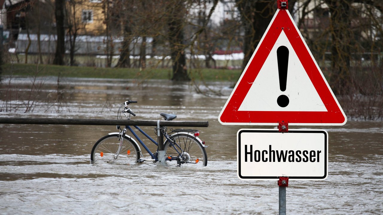 Hochwasser Gefahrenschild mit der Aufschrift "Hochwasser". Im Hintergrund sieht man Hochwasser mit einem Fahrrad