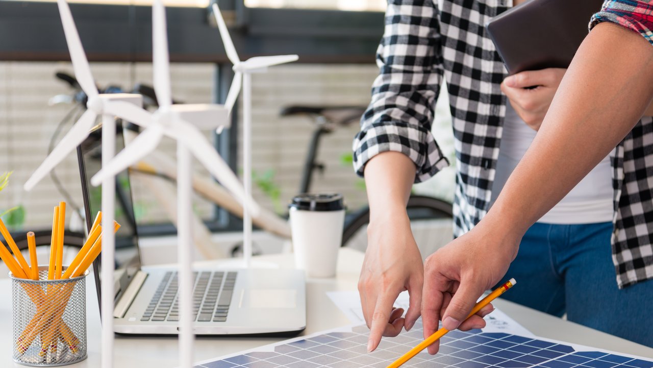 Energieingenieure diskutieren am Tisch und zeigen auf ein Solarpaneel, auf dem Tisch stehen kleine Windkraftanlagen