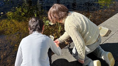 Kind und Frau sitzen am Teich und untersuchen das Wasser