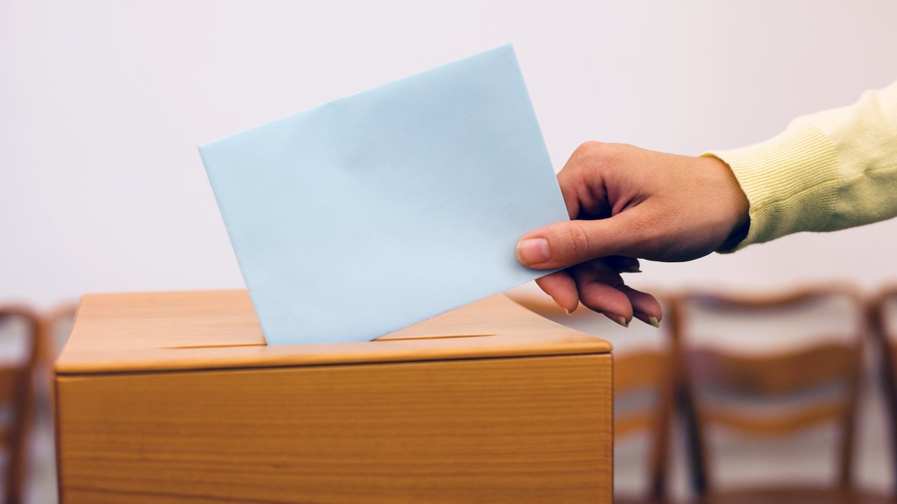 Hand wirft Zettel in Wahlurne