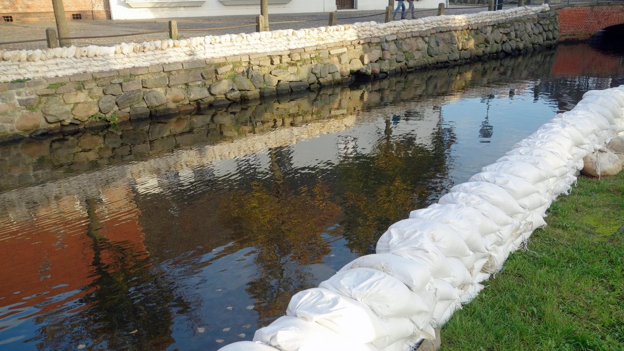 Bild zeigt Sandsäcke entlang eines Flusses zum Hochwasserschutz