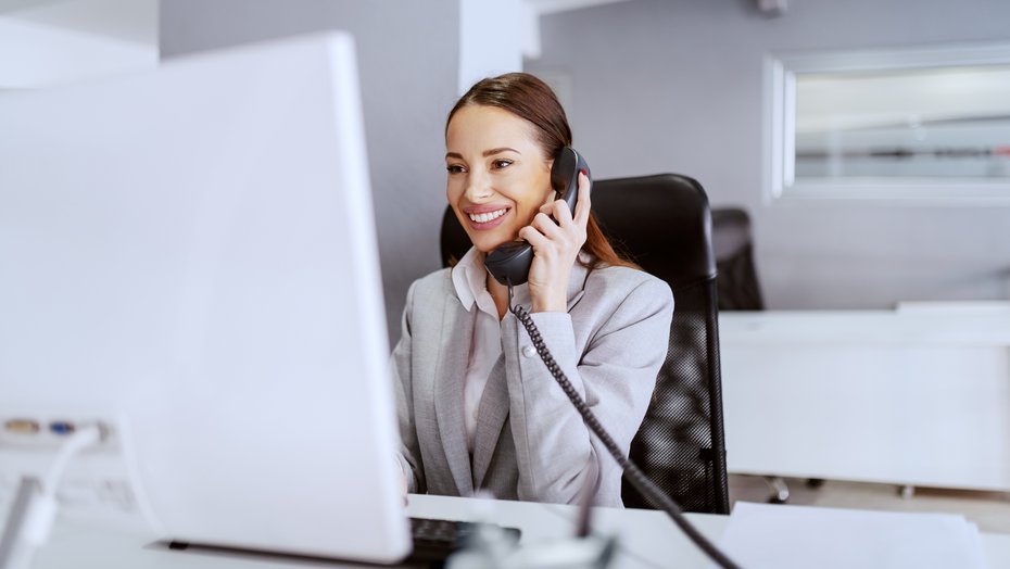 Eine Frau sitzt im Büro am Computer und telefoniert Eine Frau sitzt im Büro am Computer und telefoniert