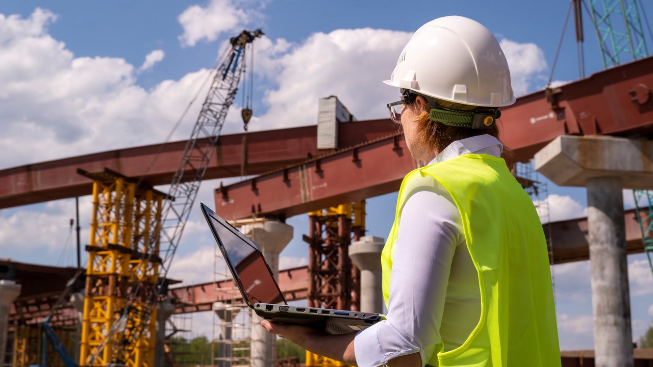 Bauingenieurin arbeitet am Laptop auf einer Brückenbaustelle.