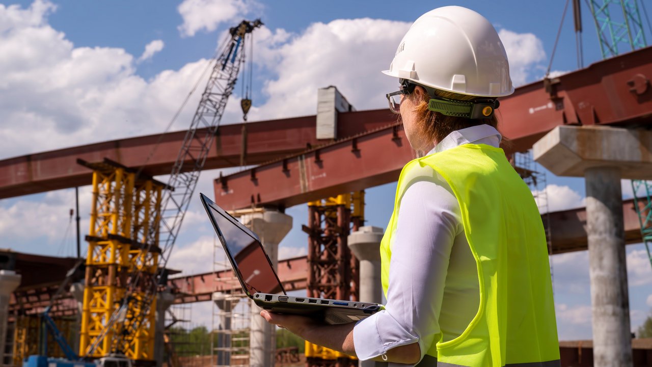 Bauingenieurin arbeitet am Laptop auf einer Brückenbaustelle.