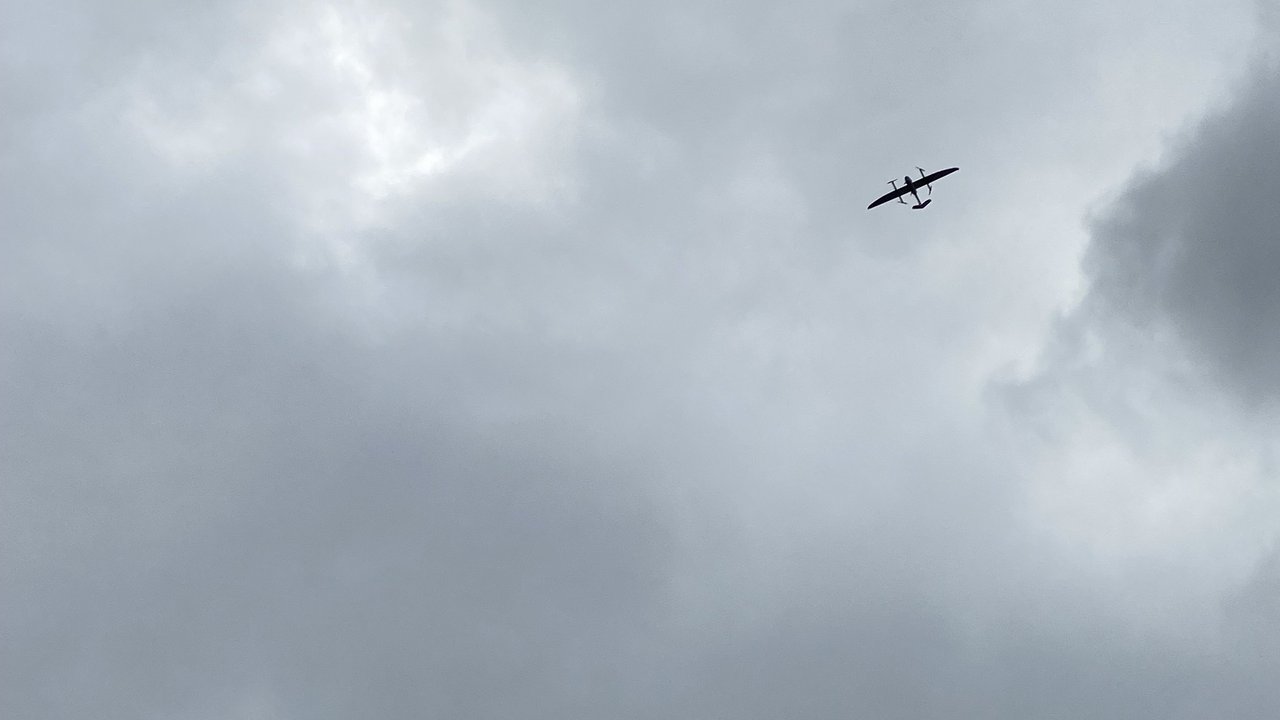 Anflug der Drohne, die eine Flügelspanne von drei Meter und ein Abfluggewicht von rund 13 Kilogramm hat. Mit einer beeindruckenden Reichweite von bis zu 100 Kilometern ist diese Drohne ideal für den Einsatz in der medizinischen Logistik. Eine Drohne vor wolkenverhangenem Himmel